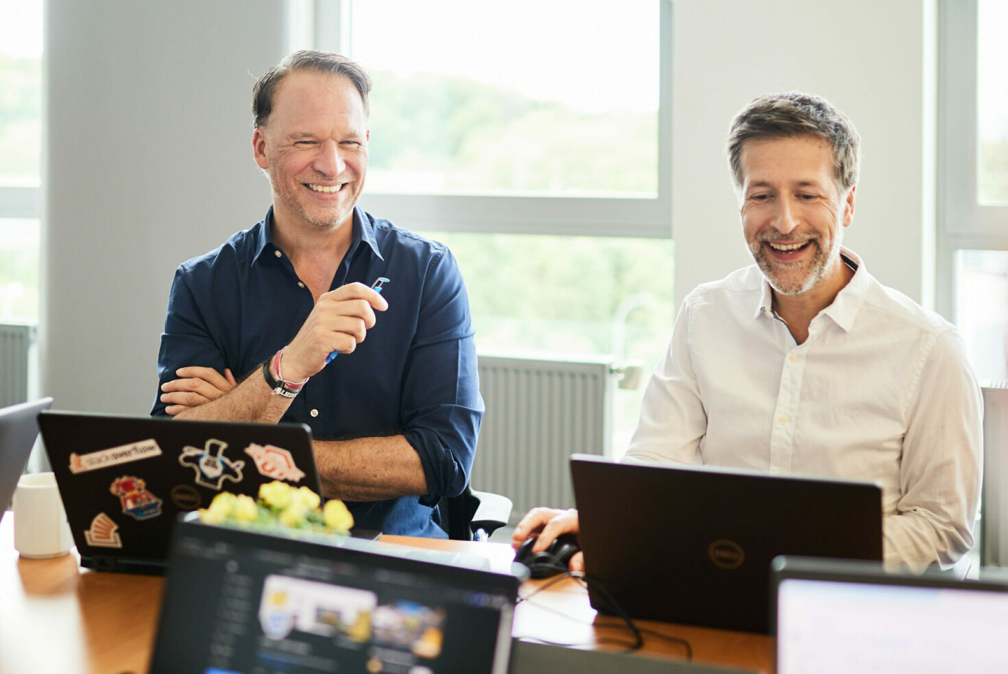 Foto von zwei Männern, die mit ihrem Laptop in einem Meeting sitzen.