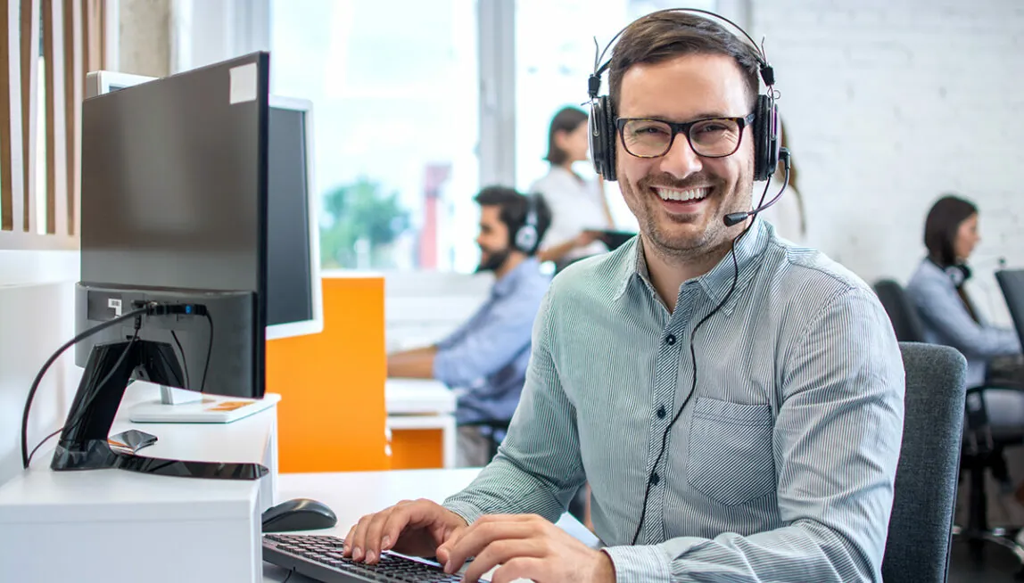 Man with headset sitting at office desk and laughing at the camera
