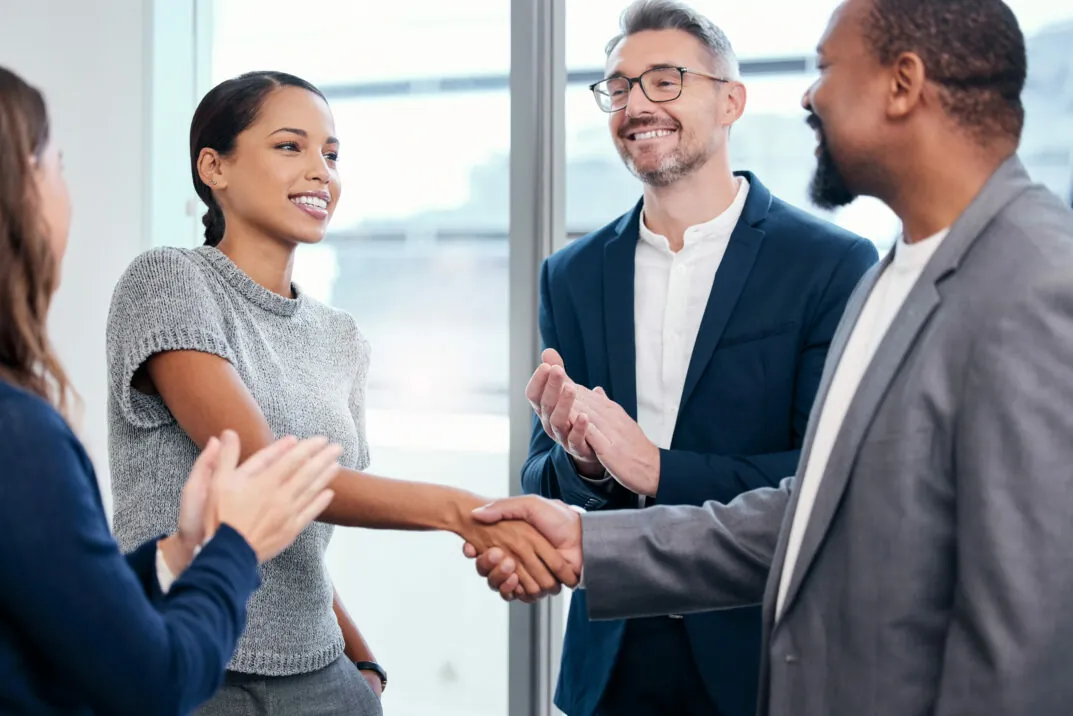 Picture of handshake between woman and man, people applauding around them