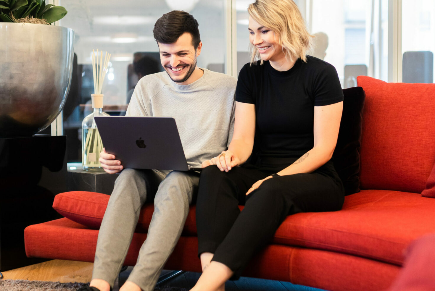 Zwei valantic-CX-Mitarbeiter*innen, die zusammen auf einem Sofa sitzen und in ein Customer-Experience-Präsentation an einem Laptop anschauen.