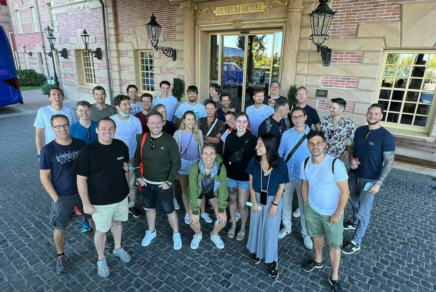 A group of approximately 30 people, both men and women, standing in front of a building labeled "Muzeum Hotel," posing for a group photo.