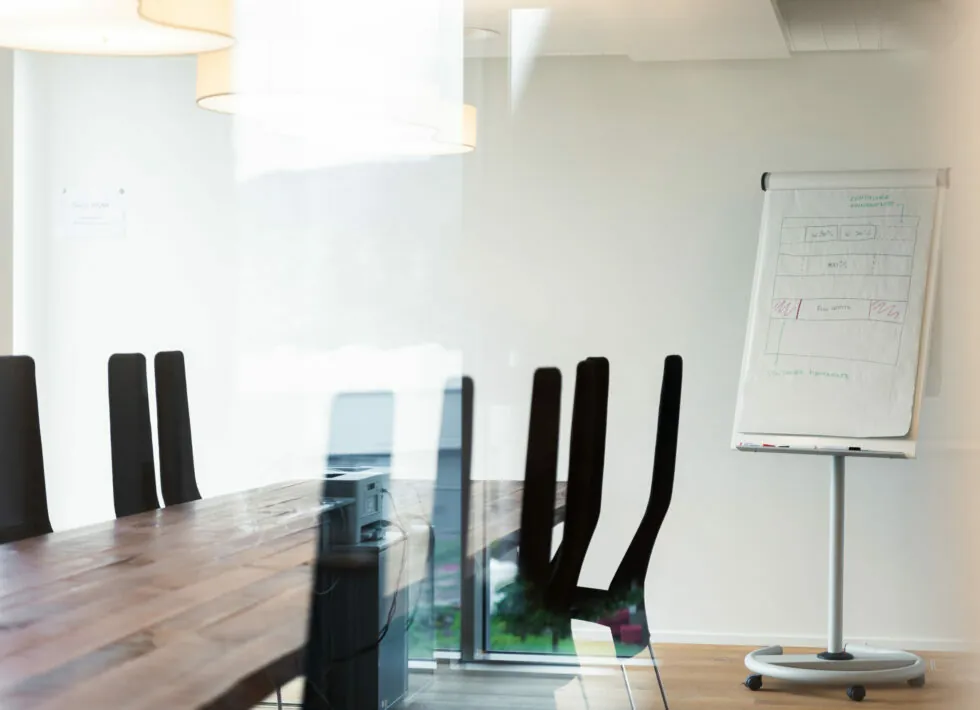 A modern conference room with a long wooden table, black chairs, and a flip chart stand displaying diagrams.
