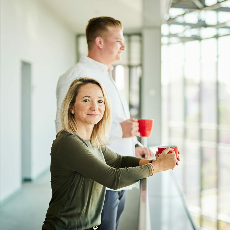A man and a woman having a cup of coffee on their office balcony.
