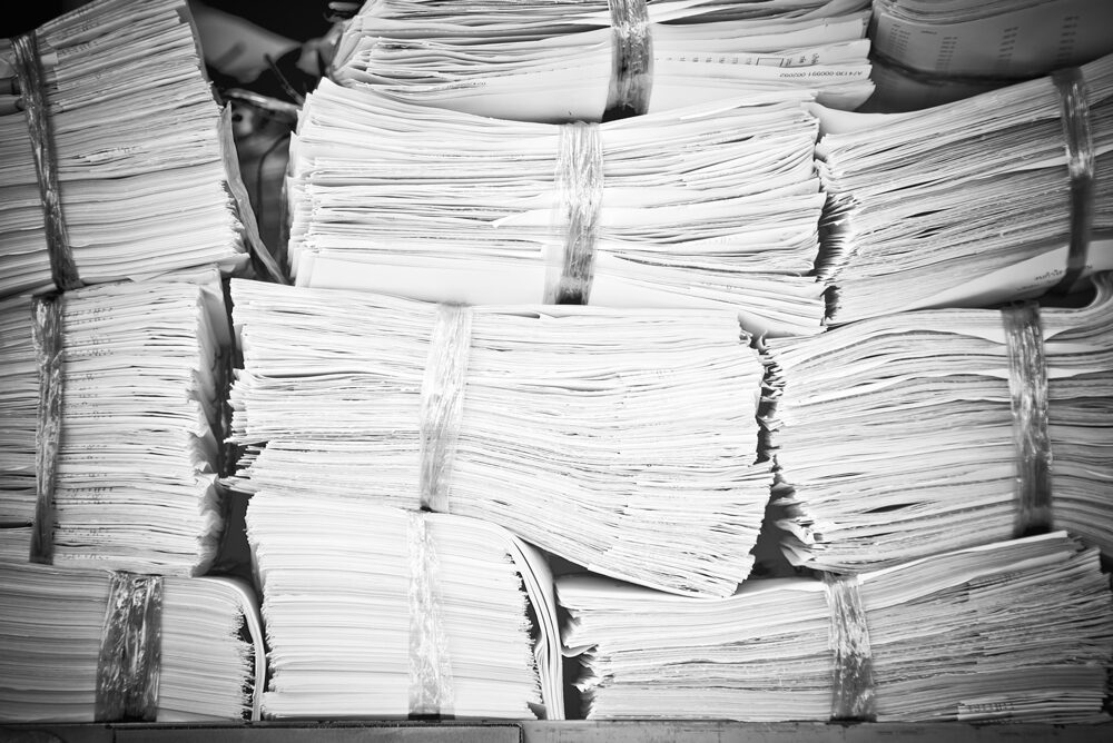 Ein Schwarzweißbild, das mehrere Bündel von Papierstapeln zeigt, die mit Schnüren zusammengebunden und dicht beieinander gestapelt sind.