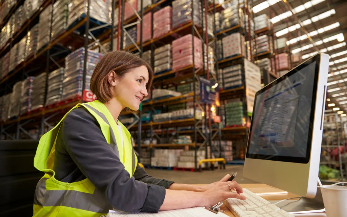 Woman with high-visibility vest at a computer in a warehouse