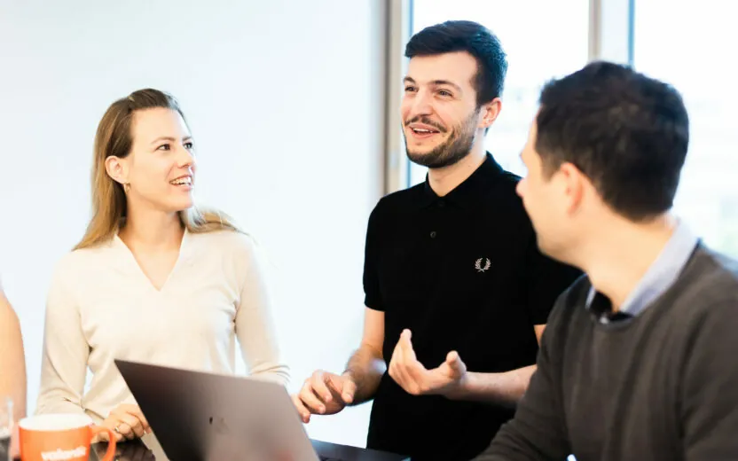 Image of a man on a laptop and a woman talking to a third, unrecognizable person.