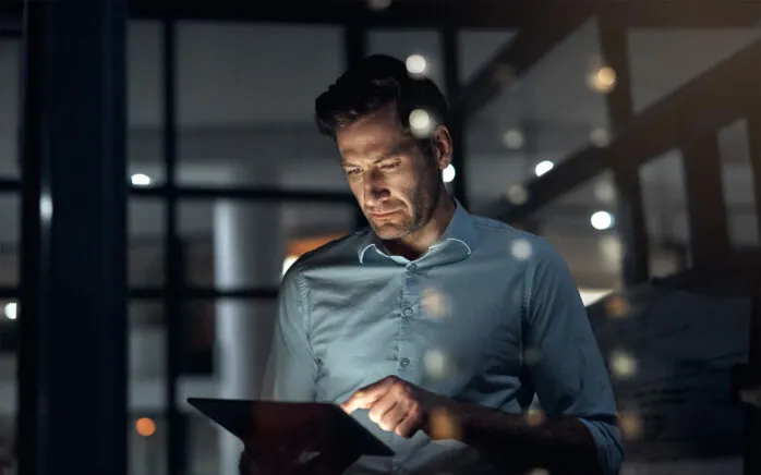 Business man, tablet and working late at night while browsing the internet, doing online research or checking trading stats. Serious entrepreneur using information technology for digital marketing