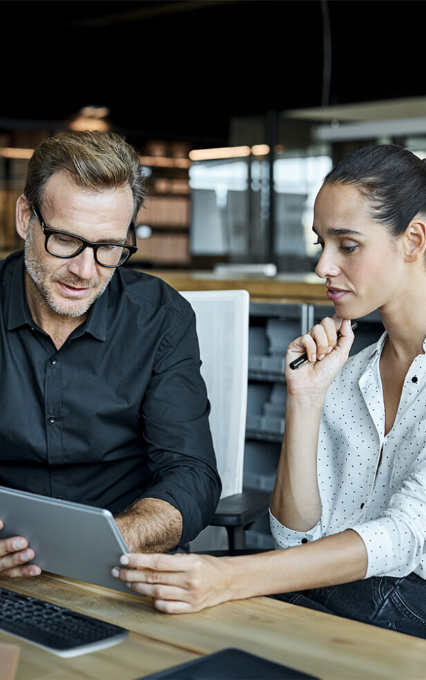 Payment Lösungen: Männliche und weibliche Kollegen betrachten einen Tablet-PC. Geschäftsleute arbeiten an einem Schreibtisch.