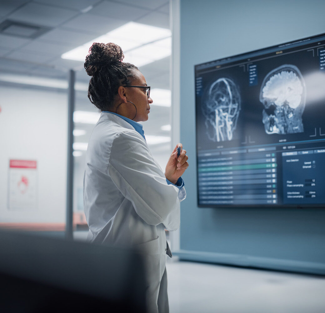 Medical Science Hospital: Confident Female Neurologist, Neuroscientist, Neurosurgeon, Looks at TV Screen with MRI Scan with Brain Images, Thinks about Sick Patient Treatment Method. Saving Lives