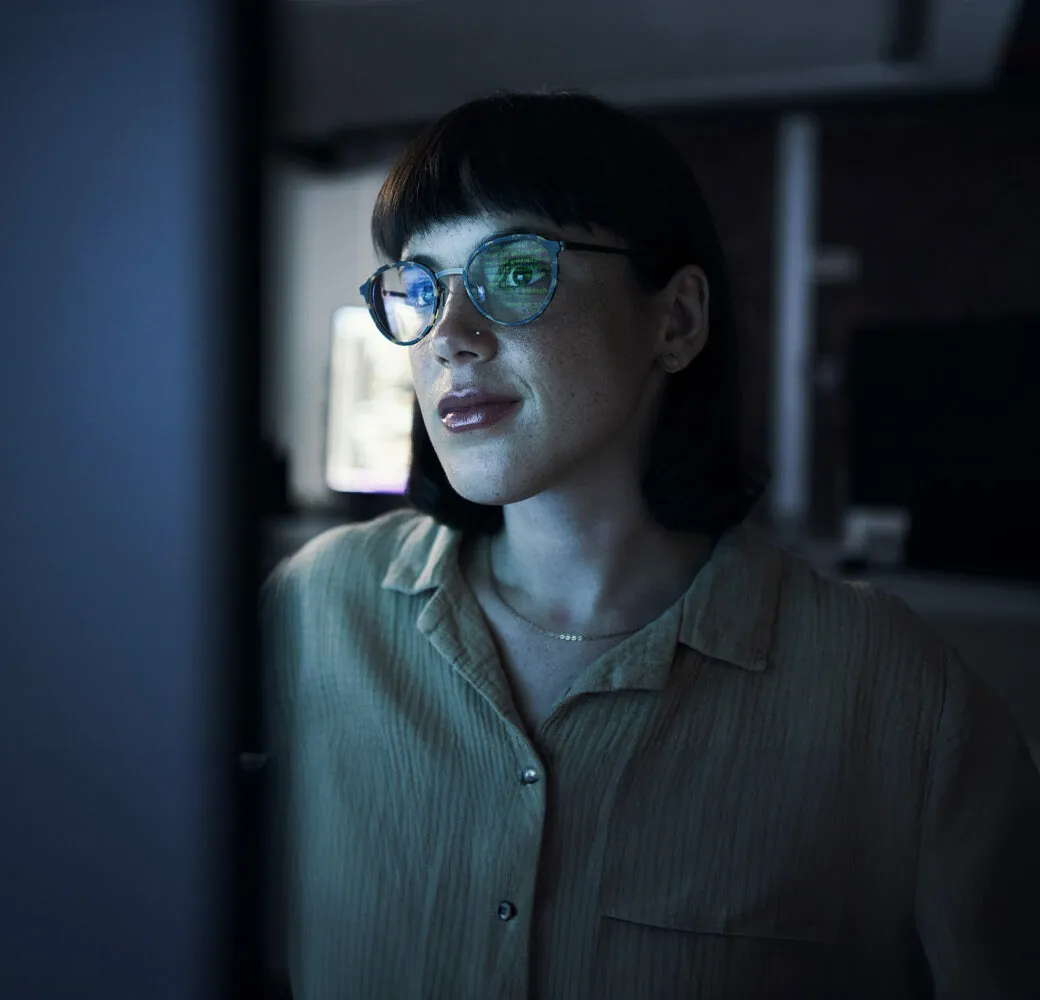 Woman with glasses looking at a computer screen at night