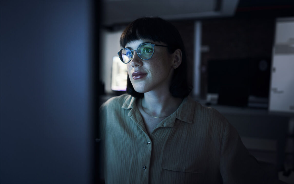 Woman with glasses looking at a computer screen at night