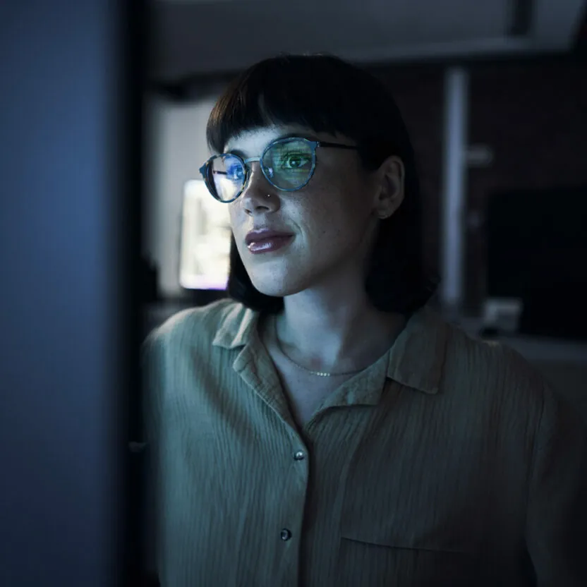 Woman with glasses looking at a computer screen at night