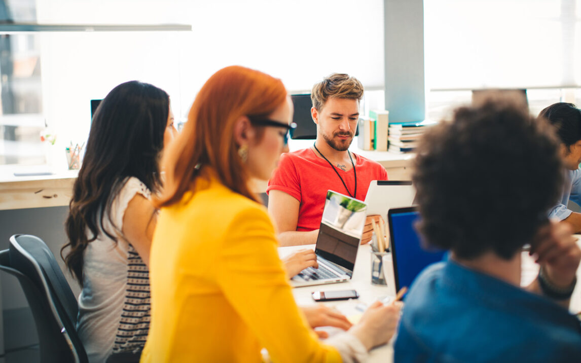 Start up team having a meeting in the office and planning a new project. Sitting by the table, using laptops, digital tablets, notes. Talking and brainstorming. Multi-Ethnic Group.Wearing casual clothes. | Training Center
