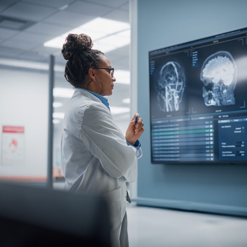 Medical Science Hospital: Confident Female Neurologist, Neuroscientist, Neurosurgeon, Looks at TV Screen with MRI Scan with Brain Images, Thinks about Sick Patient Treatment Method. Saving Lives
