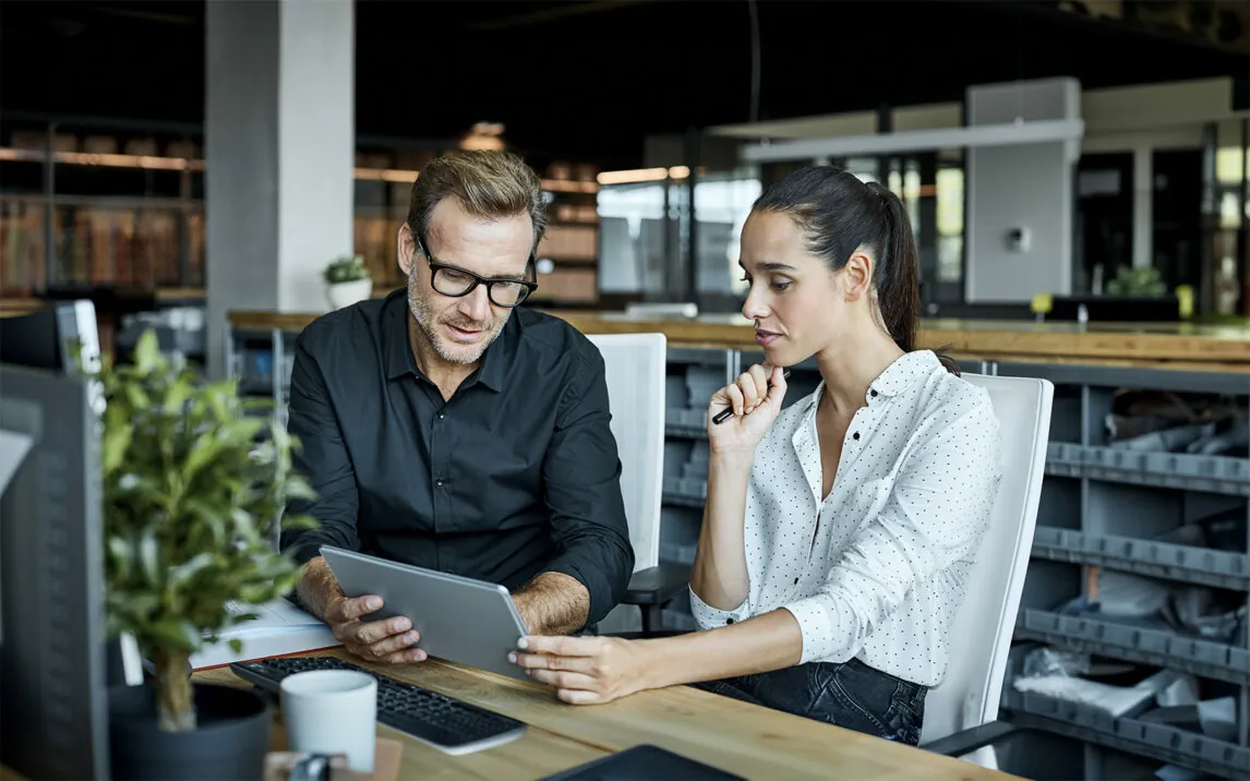 Male and female colleagues looking at tablet PC. Business people are working at desk.