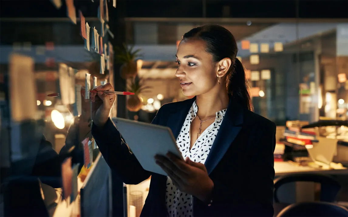 Shot of a young businesswoman writing adhesive notes on a glass wall while walking late in her office