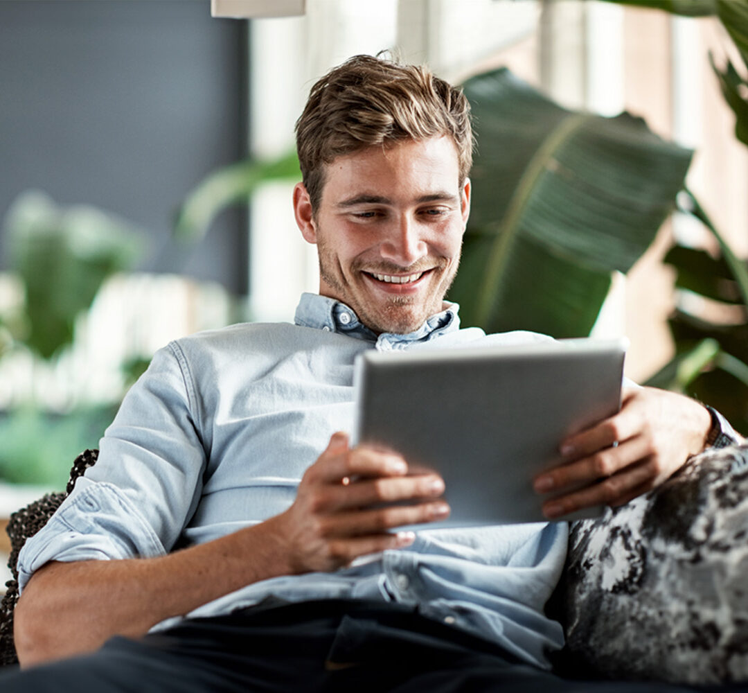Shot of a happy young man using his tablet while relaxing on the couch at home