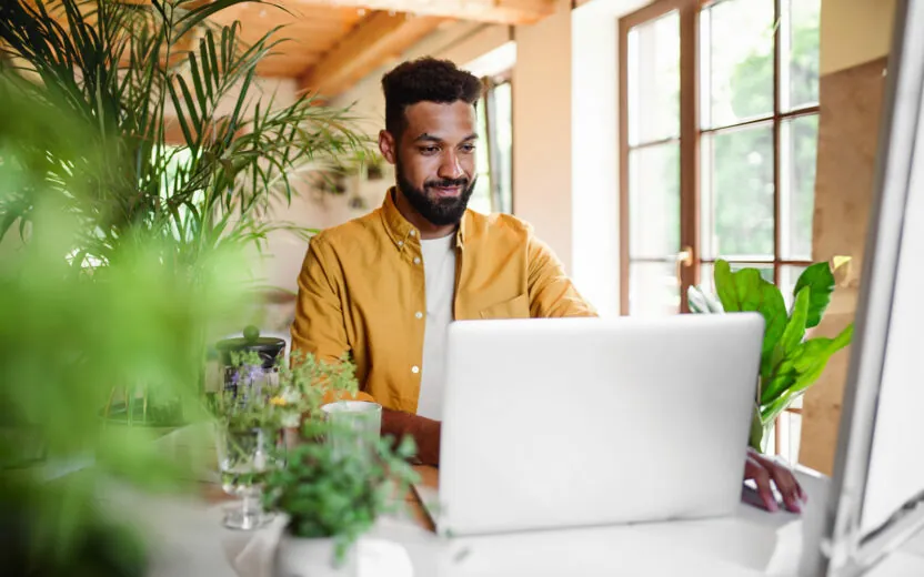 A young man with laptop and coffee working indoors, home office concept.