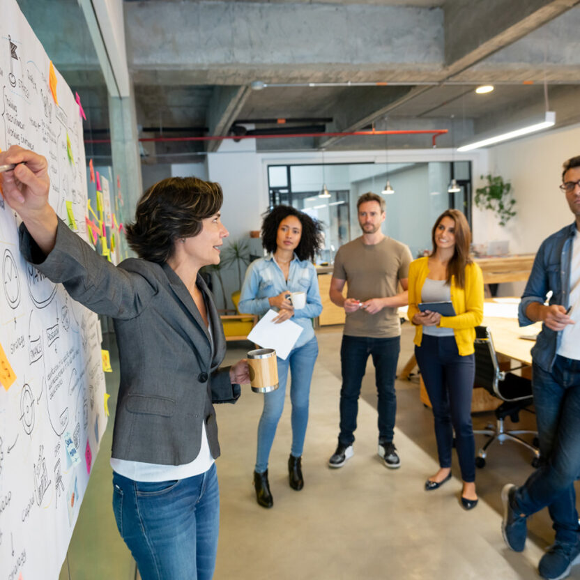 Woman making a business presentation in a meeting at a creative office and pointing to her team her business plan