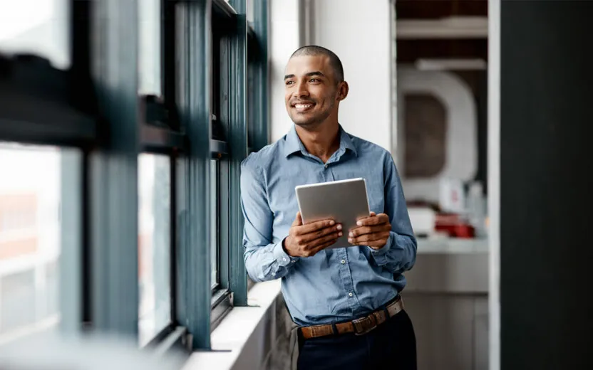 Shot of a young businessman using a digital tablet while standing at a window in an office