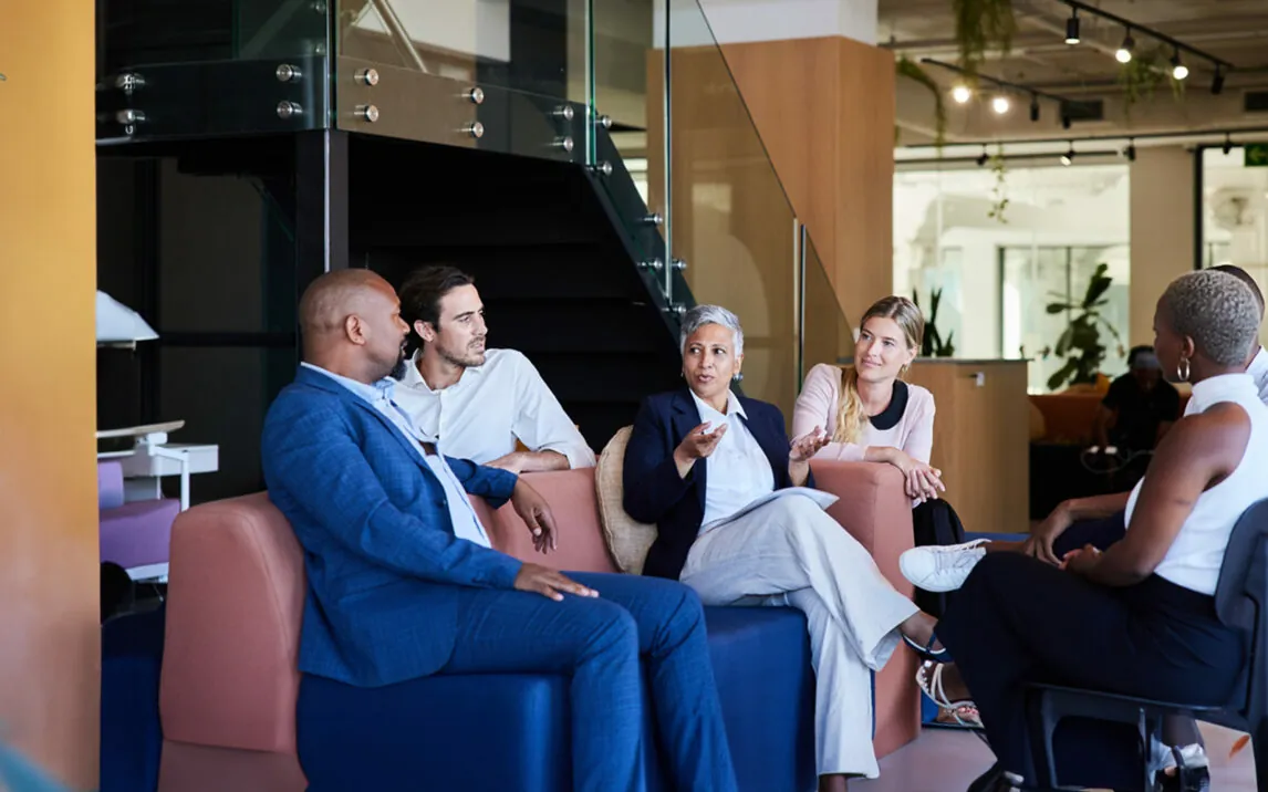 Diverse group of smiling businesspeople talking together during a casual meeting in the lounge area of a modern office