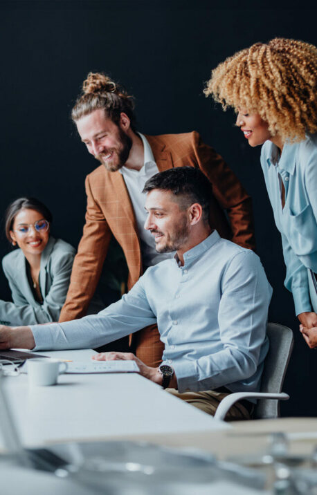 Team of four colleagues using a laptop computer together at office desk and talking about SAP S/4HANA.