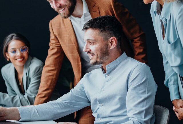 Team of four colleagues using a laptop computer together at office desk and talking about SAP S/4HANA.