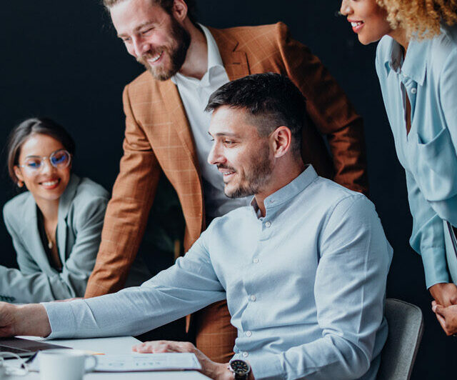 Team of four colleagues using a laptop computer together at office desk and talking about SAP S/4HANA.