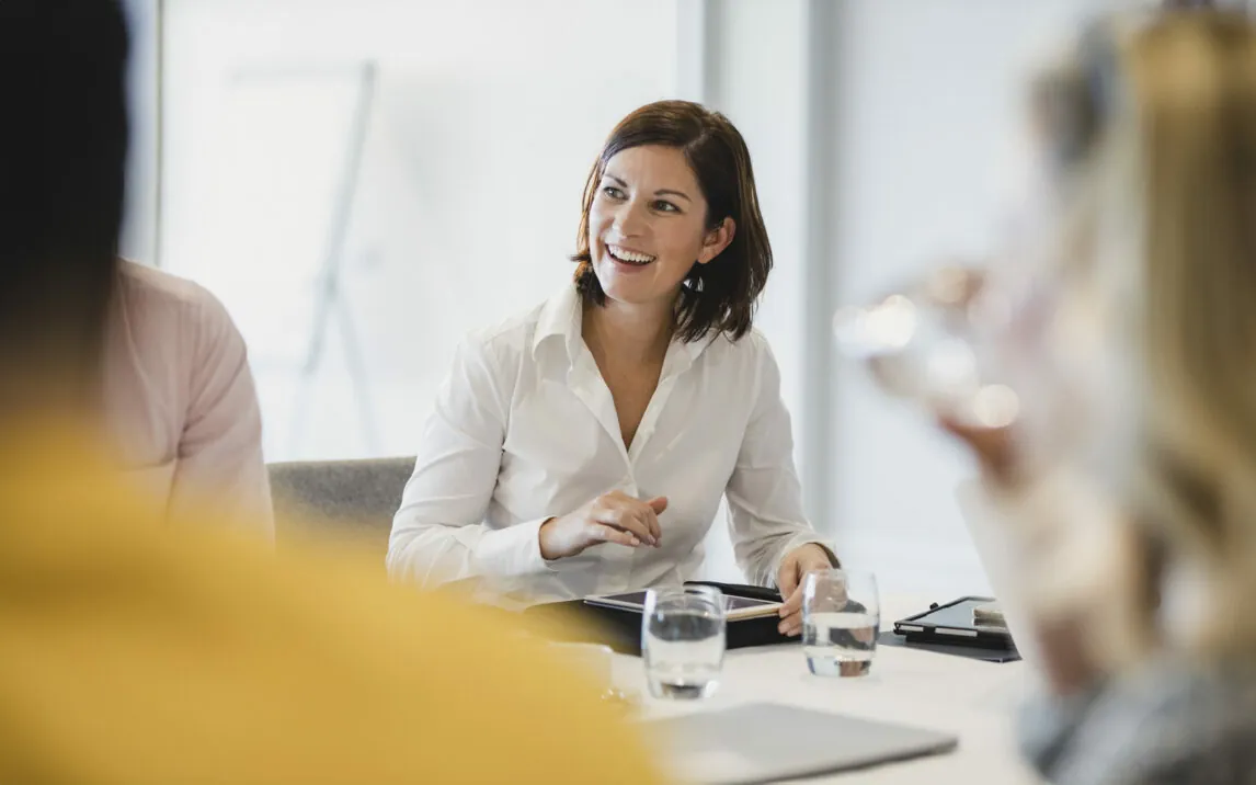 Businesswoman smiling at meeting table, listening, learning, success, happiness