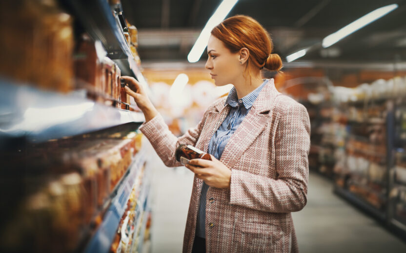 Mulher jovem a segurar um jarro de tomate seco num supermercado, à procura de uma marca especifica