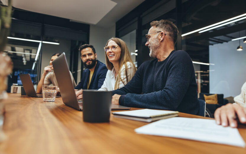 Grupo de empresários bem sucedidos a fazer um briefing numa sala de reuniões. Empresários felizes a sorrir enquanto trabalham juntos num local de trabalho moderno. Diversos colegas de trabalho a colaborar num projeto.