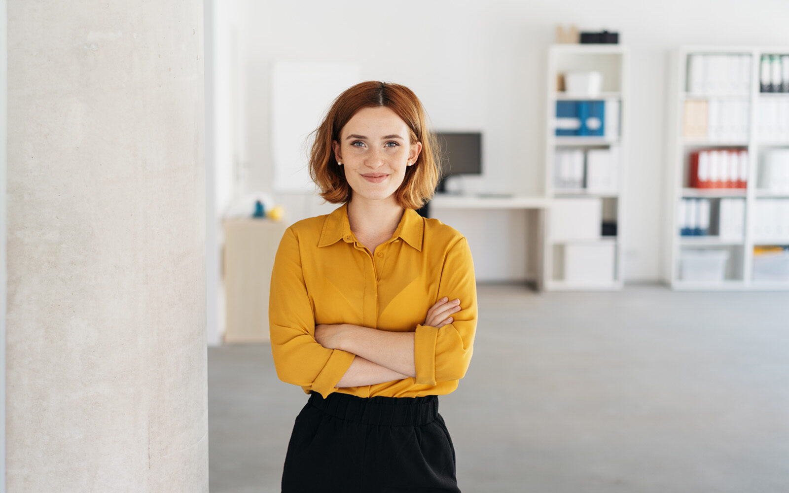Happy, relaxed, confident businesswoman with folded arms, smiling in a spacious office.