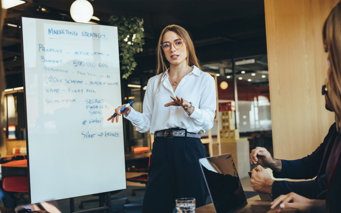 Smart businesswoman discussing her marketing ideas with her team in a modern workspace. Confident young businesswoman giving a presentation during a meeting with her colleagues.