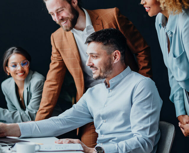 Team of four colleagues using a laptop computer together at office desk.