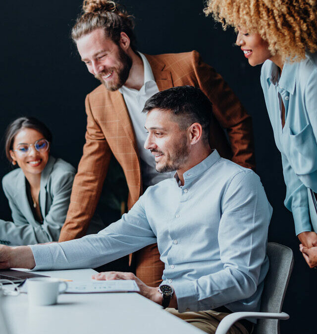 Equipa de quatro colegas que utilizam um computador portátil juntos na secretária do escritório.