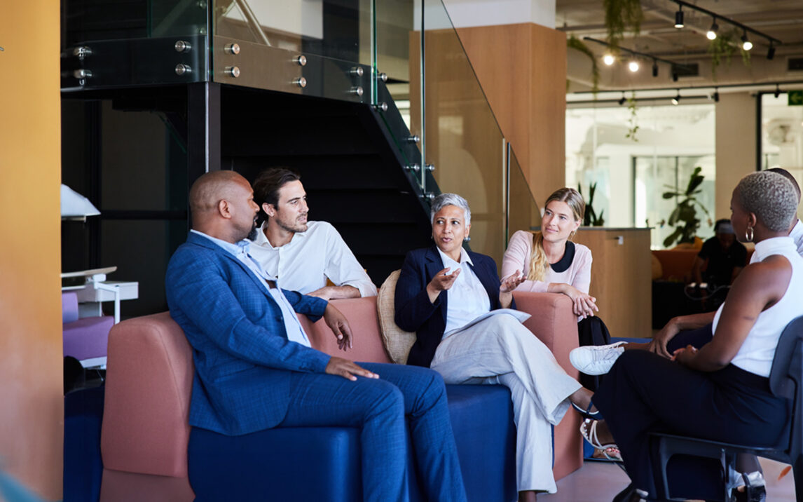 Grupo diversificado de empresários sorridentes a conversar durante uma reunião informal na área comum de um escritório moderno