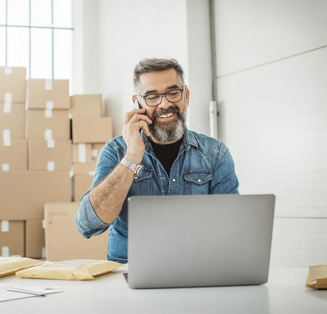Bearded men working on packaging and online delivery in home office business. He talking on phone with customer