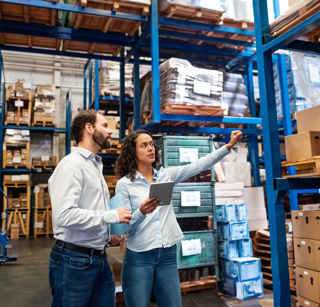 Businesswoman with a digital tablet showing and talking with male worker in distribution warehouse. Manager working with foreman in warehouse checking stock levels.