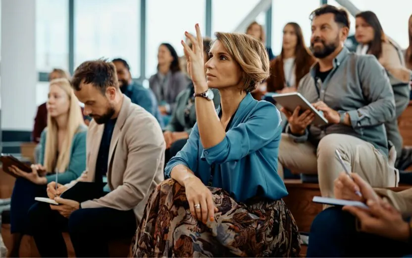 Female entrepreneur raising her hand to answer a question during business conference in convention center.