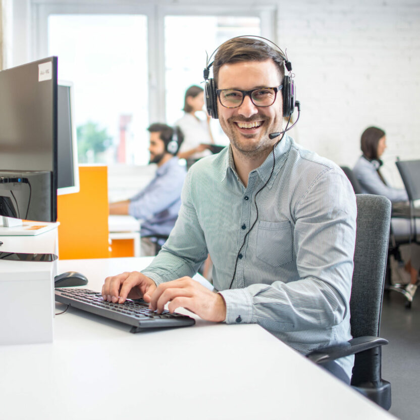 Male customer support telephone operator with headset in call centre. Group of sales representatives working in the office.