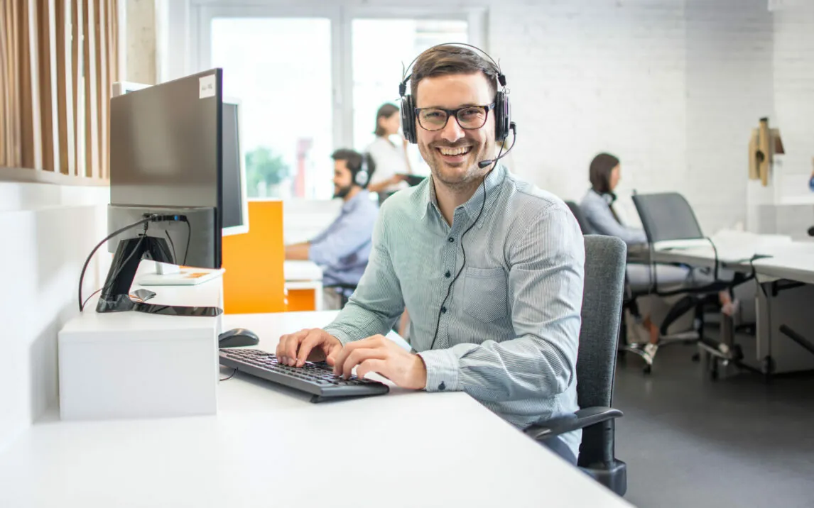 Male customer support telephone operator with headset in call centre. Group of sales representatives working in the office.