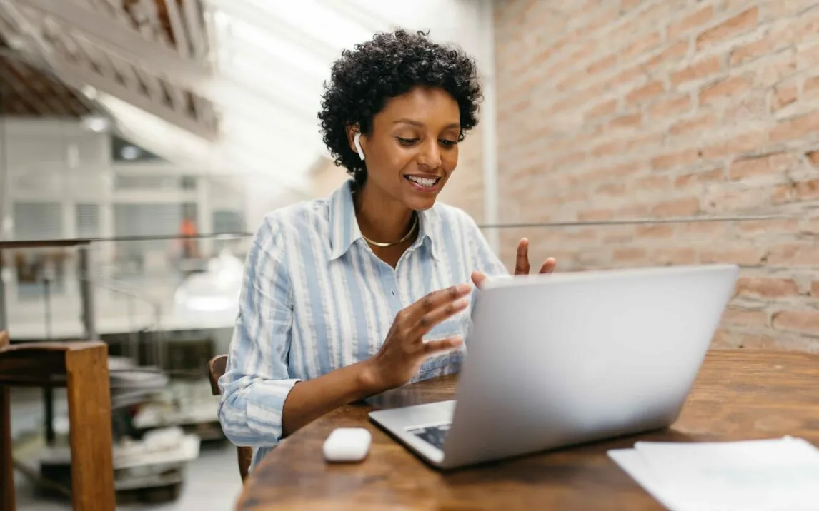 small business owner having an online meeting in a warehouse. Female entrepreneur video calling her business partners on a laptop. Happy businesswoman running an online startup.