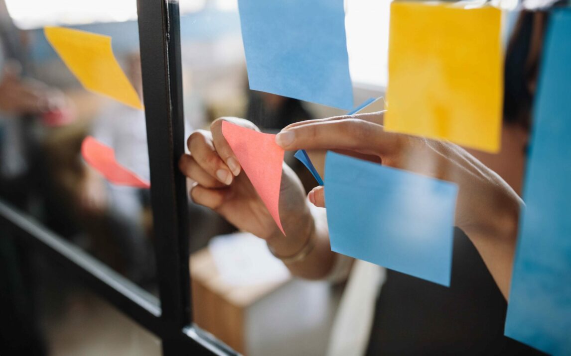 Close up shot of hands of woman sticking adhesive notes on glass wall in office