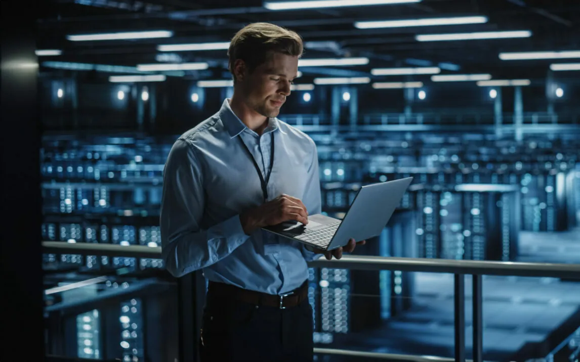 Data Center Specialist Engineer Using Laptop Computer. Server Farm Cloud Computing Facility with Male Maintenance Administrator Working. Data Protection Network for Cyber Security.