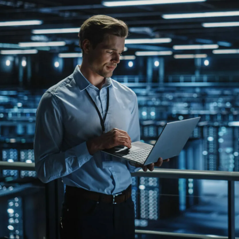 Data Center Specialist Engineer Using Laptop Computer. Server Farm Cloud Computing Facility with Male Maintenance Administrator Working. Data Protection Network for Cyber Security.