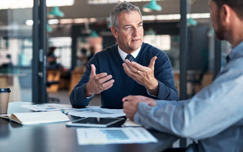 Dois homens a analisar dados com ficheiros e um tablet na mesa