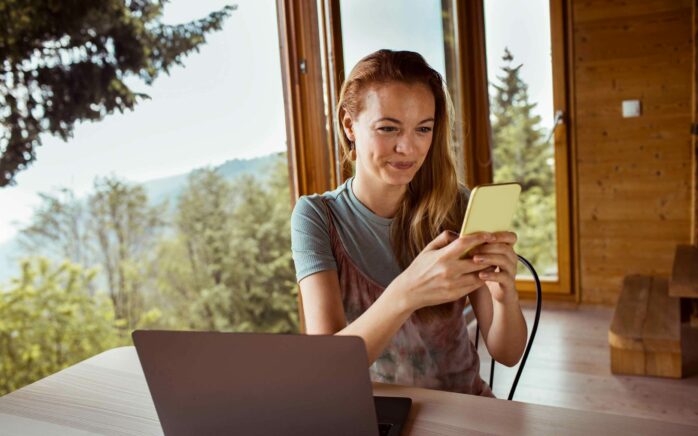Close up of a mid adult woman using a phone while spending time in her cabin in the woods