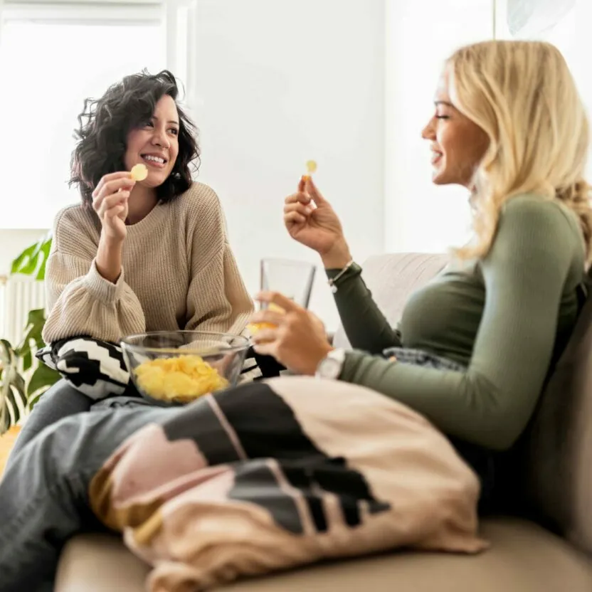 Friends sitting on sofa eating potato chips