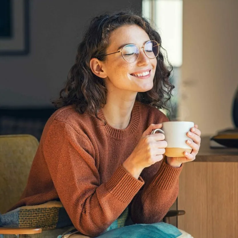 Happy young woman drinking a cup of tea or coffee in an autumn morning.