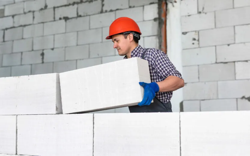 Man wearing a red helmet working, building a wall from bricks.